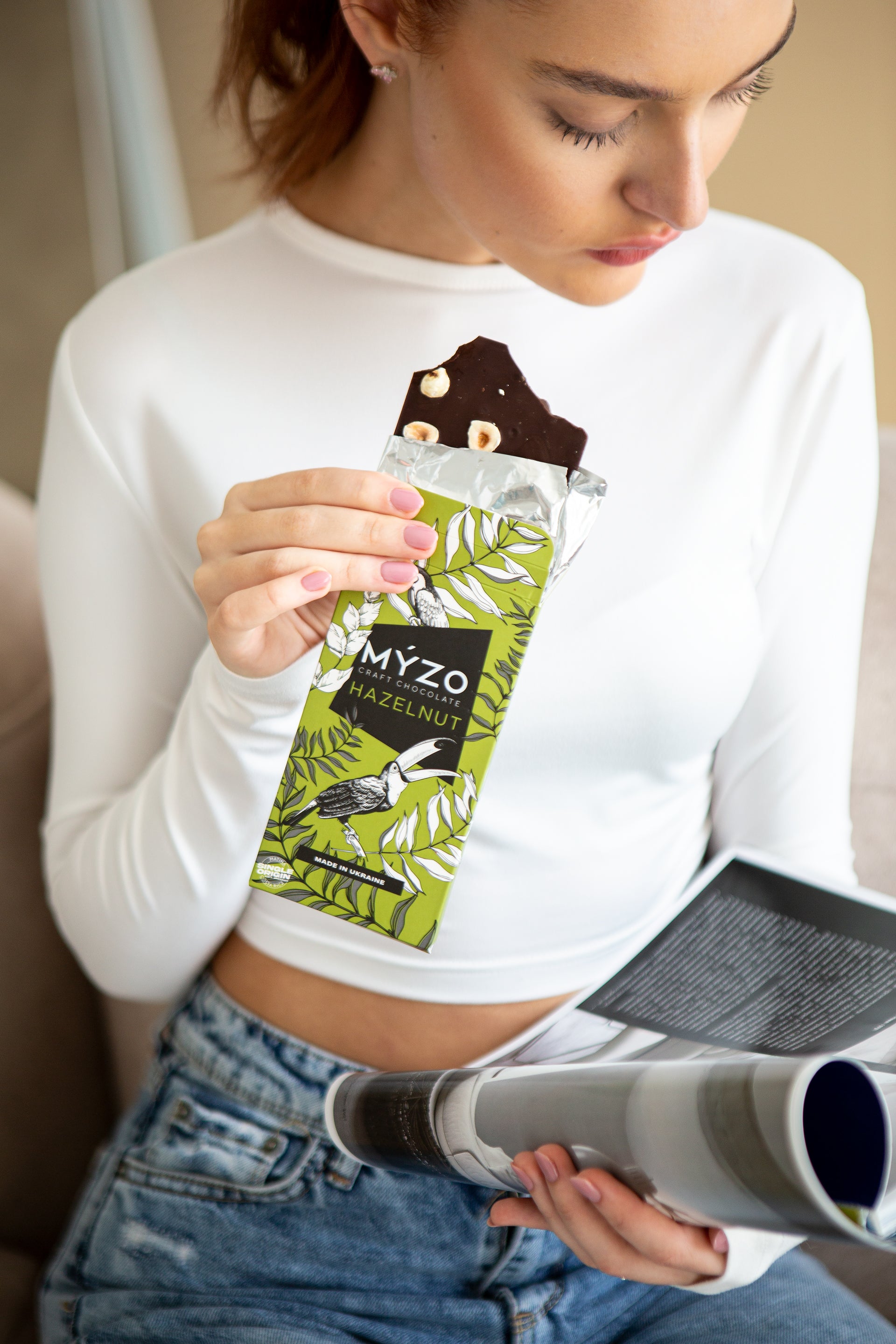 Дівчина їсть Myzo з ліщиною і читає журнал