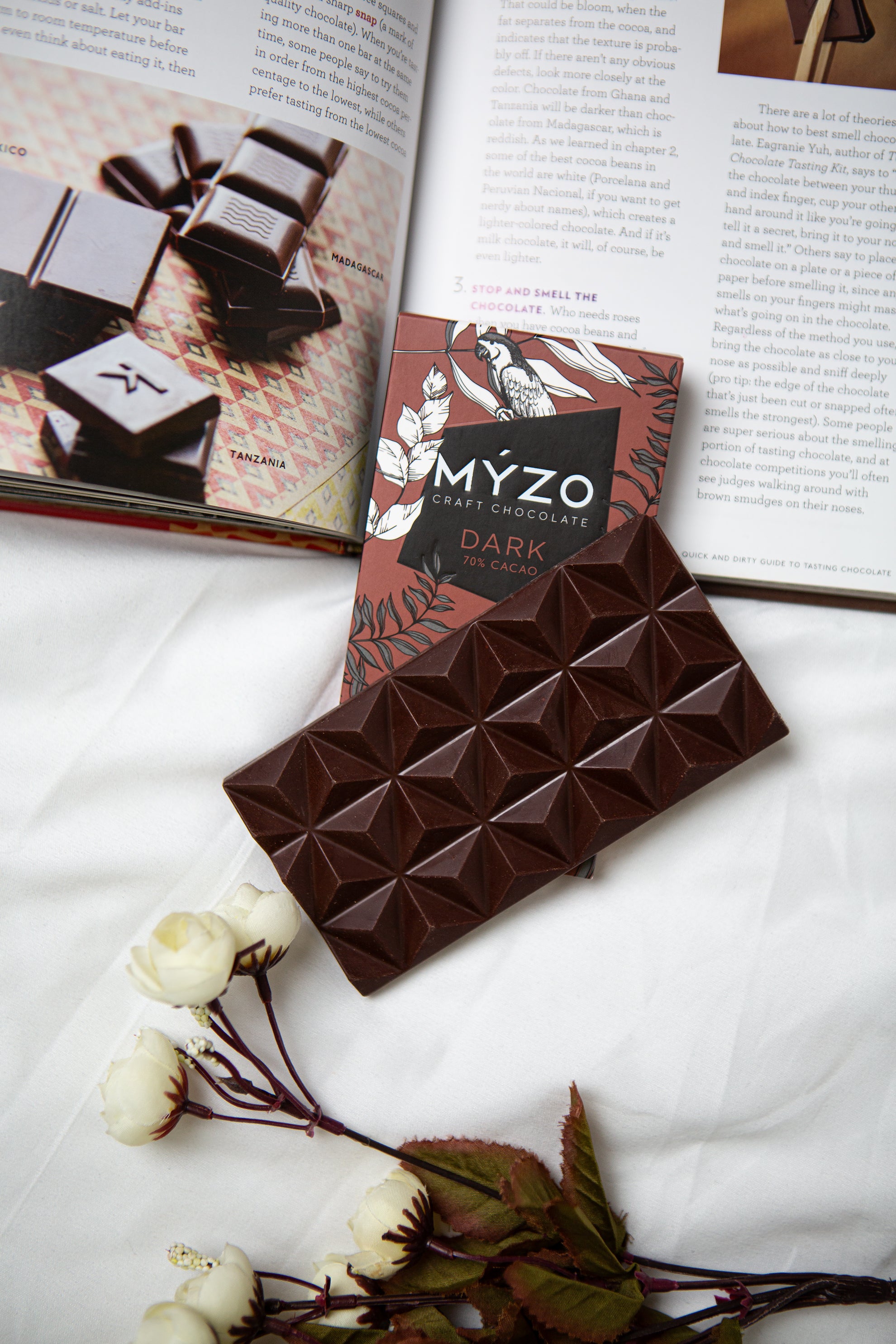Myzo 70% чорний шоколад лежить на книзі з квіткою