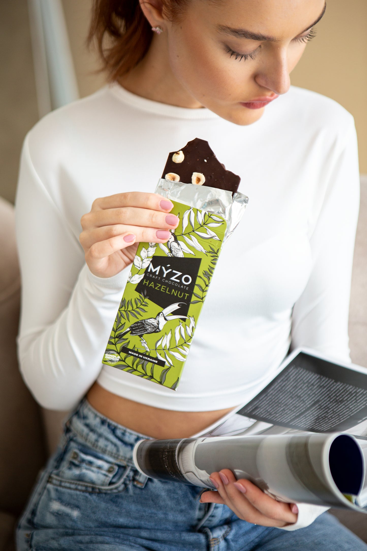 Дівчина їсть Myzo Chocolate з ліщиною і читає журнал